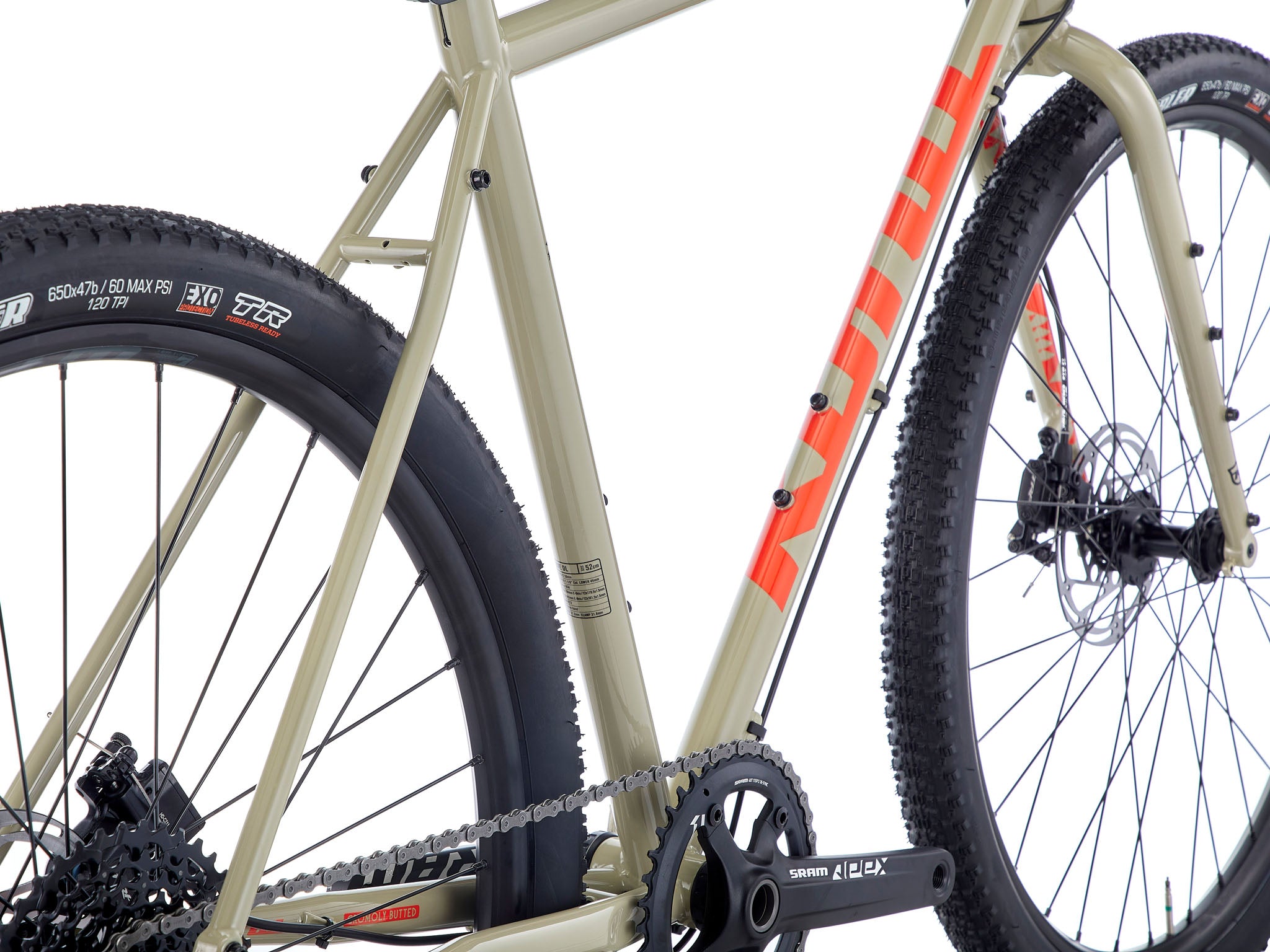 Side view of the Rove DL steel gravel bike on a forest trail, showcasing its rugged frame and all-terrain tires.